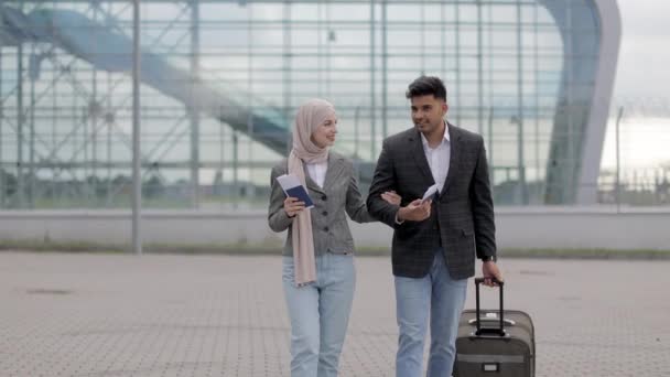 Mujer musulmana en hiyab y hombre árabe, caminando al aire libre llevando una maleta y hablando — Vídeo de stock