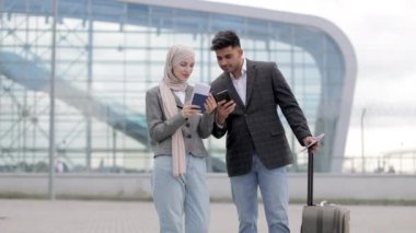 Bavullu Müslüman çift, havaalanında dikilip uçuş saatlerini kontrol ediyorlar.