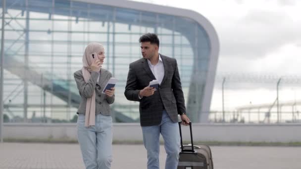 Senhora muçulmana em hijab, e homem árabe, transportando mala fora do aeroporto, segurando passaportes e bilhetes — Vídeo de Stock