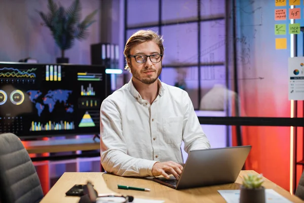 Pria berkacamata duduk di kantor dan menggunakan laptop nirkabel — Stok Foto