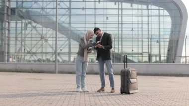 Müslüman kadın tesettürlü ve Arap adam, mutlu ve birlikte atlıyorlar, modern havaalanının önünde duruyorlar.