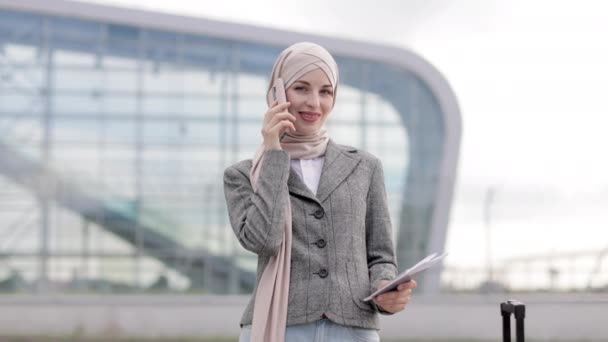 Αραβίδα επιχειρηματίας με μαντίλα, στέκεται με τηλέφωνο, διαβατήριο και βαλίτσα έξω — Αρχείο Βίντεο