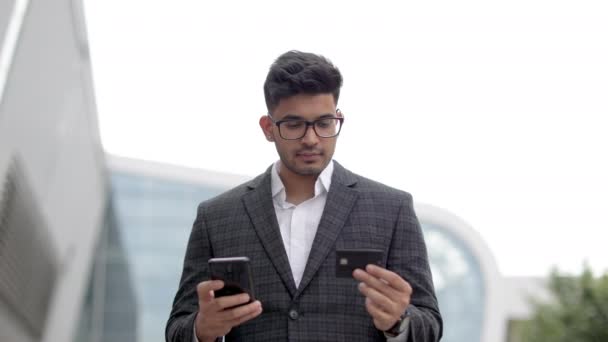 Hezký mladý indián v brýlích, pomocí chytrého telefonu a držící kreditní kartu — Stock video