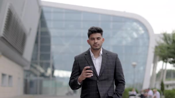 Арабский бизнесмен, стоящий перед аэропортом и пьющий кофе перед деловой поездкой — стоковое видео
