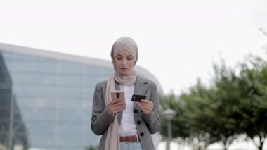 Müslüman iş kadını sokakta duruyor ve kredi kartıyla alışveriş yapıyor.