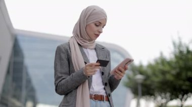 Başörtülü Müslüman kadın cep telefonu kullanıyor, kredi kartı tutuyor, online ödeme yapıyor.