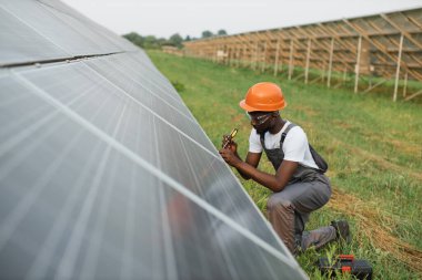 Üniformalı adam güneş panellerini tamir etmek için tornavida kullanıyor.