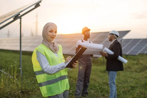 Woman in hijab using clipboard for work at solar station
