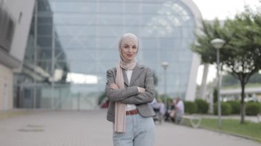 Müslüman kadın, modern binanın arka planında kollarını kavuşturarak duruyor.