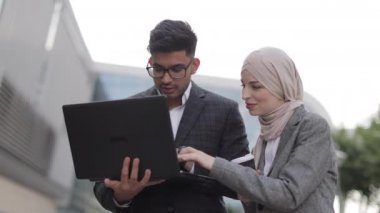 Arap erkek ve Müslüman kadın tesettürde çalışırken konuşuyor ve gülümsüyor, şehir merkezinin yakınında bir kahve molası veriyor, dizüstü bilgisayar kullanıyor ve ortak projeyi tartışıyorlar..