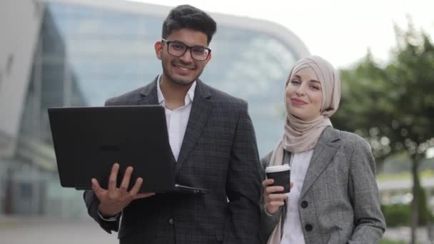 Geschäftsleute mit Laptop und Kaffee im Freien. Schöner indischer Mann und muslimische Dame posieren vor der Kamera vor dem Business Center, benutzen Laptop und trinken Kaffee. — Stockvideo