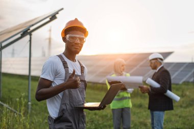 Güneş istasyonunda elinde dizüstü bilgisayarla duran teknisyen.