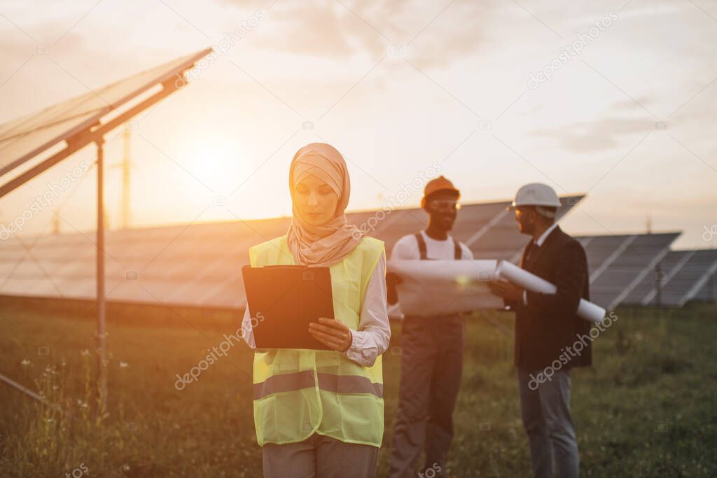 Woman in hijab writing on clipboard at solar station