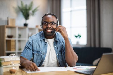 Masada otururken kameraya gülümseyen kulaklı bir adam.