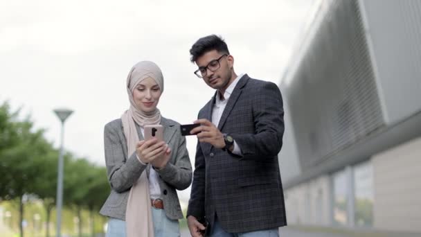 Арабские мусульмане удовлетворены деловой парой, стоящей на открытом воздухе рядом с современным зданием и осуществляющей онлайн-оплату с помощью кредитной карты и смартфона. Проверка баланса счета, покупка концепции товара. — стоковое видео