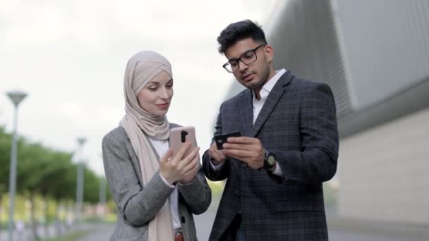 Sourire satisfait couple d'affaires multiracial achetant en ligne avec carte de crédit debout à l'extérieur du terminal de l'aéroport. Joyeux jeunes collègues appréciant le magasinage en ligne de billets pour un voyage d'affaires. — Video