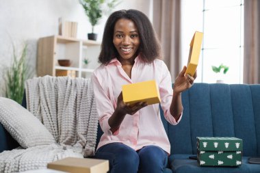 Kanepede otururken Afrikalı Amerikalı kadın hediye kutusunu açıyor.