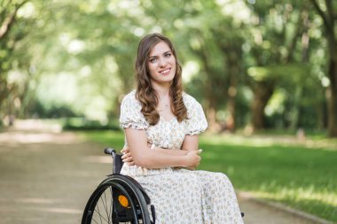 Yeşil park arasında gülümseyen fiziksel engelli bir kadın.