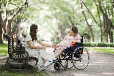 Parkta tekerlekli sandalye kullanan bir kadın arkadaşının elini tutuyor.