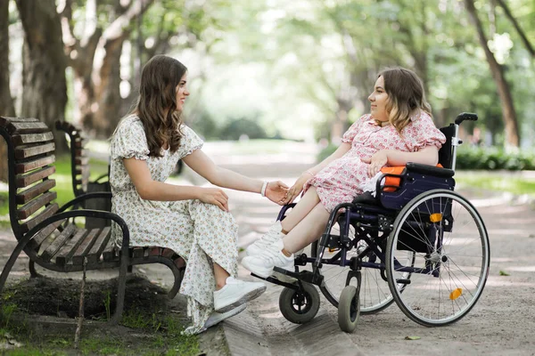Γυναίκα στο πάρκο κρατώντας φίλους χέρι που χρησιμοποιούν αναπηρική καρέκλα — Φωτογραφία Αρχείου