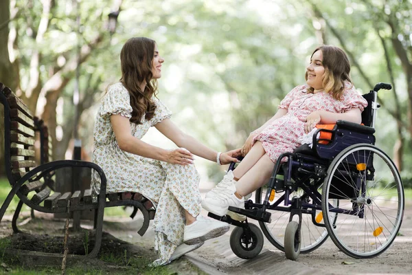 Frau im Park hält Freundin im Rollstuhl an der Hand — Stockfoto