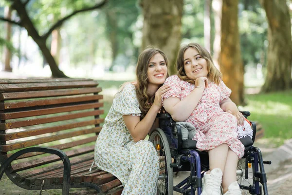 Bankta oturan ve özürlü arkadaşına sarılan bir kadın.