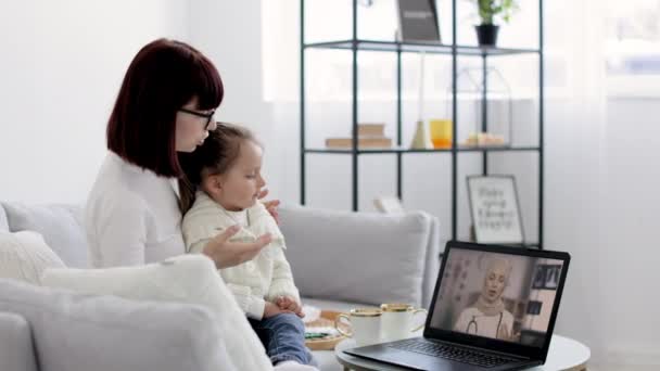 Kobieta mama w lekkich ubrań z chorym dzieckiem dziewczynka pacjenta rozmawia online z kobietą muzułmańskiego lekarza — Wideo stockowe