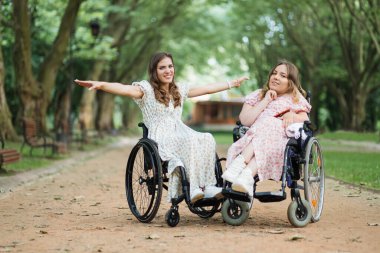 Parkta kameraya poz veren tekerlekli sandalyeli mutlu bayanlar.