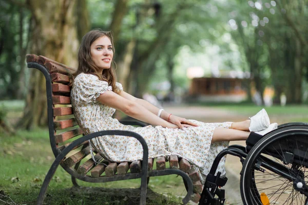 Woman keeping feet on wheelchair while sitting on bench — Stockfoto