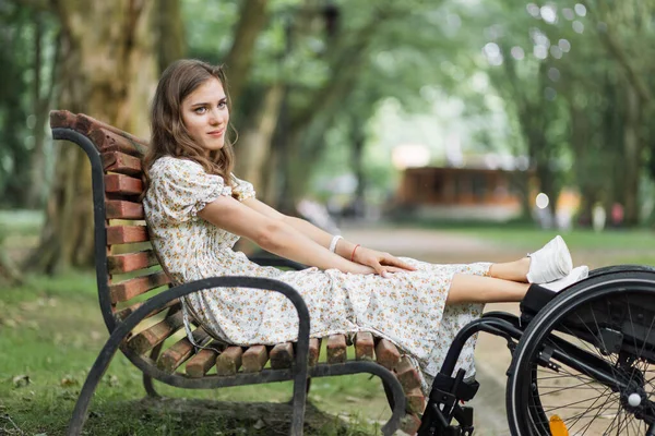 Woman keeping feet on wheelchair while sitting on bench — Stockfoto