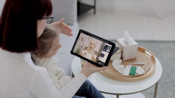 Médecin thérapeute consultation jeune femme et sa fille lors d'un rendez-vous en ligne sur tablette à la maison. — Video