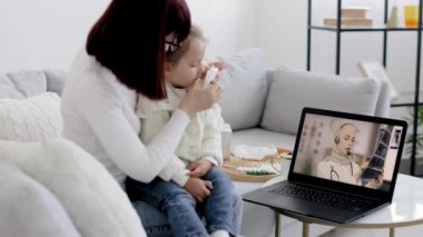 Anne ve küçük kızı, evde kendine güvenen kadın Arap doktoruyla video görüşmesi yapıyorlar.
