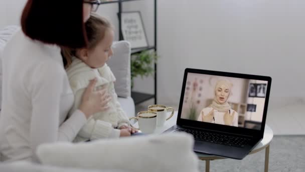Врач-терапевт консультирует молодую женщину и ее дочь во время онлайн-встречи на ноутбуке на дому. — стоковое видео