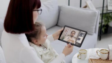 Annemin hasta bir kızın sıcaklığını ölçtüğü ve elinde haplar olan erkek doktorla görüntülü konuşma yaptığı görüntüler.