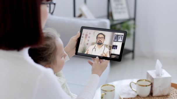 Primer plano por encima de la vista del hombro de la pantalla digital de la tableta con guapo médico masculino de 30 años en auriculares, dando consulta en línea — Vídeo de stock