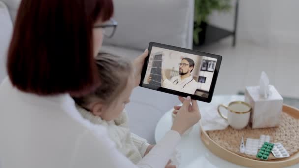 Back view of Mother and little daughter with running nose and having video chat with male doctor on tablet at home — Stockvideo