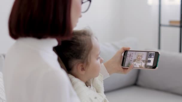 Vista do ombro da mãe medindo a temperatura da menina doente, tendo a consulta vídeo com o médico árabe fêmea — Vídeo de Stock