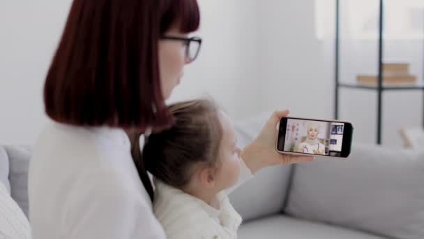 Madre e hija pequeña con nariz hueca haciendo videollamadas en casa con su doctora árabe confiada — Vídeos de Stock