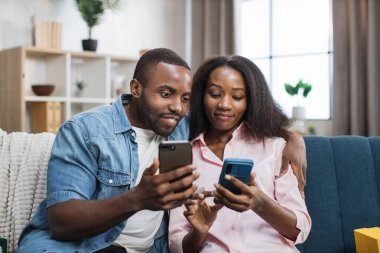 Mutlu çift ellerinde akıllı telefonlarla kanepede dinleniyor.