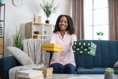 Kanepede otururken elinde hediye kutusu tutan mutlu Afrikalı kadın.