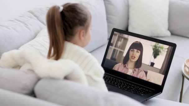 Vista posteriore della giovane ragazza seduta e rilassante sul divano a casa e che parla in videochiamata con madre sorridente. — Video Stock
