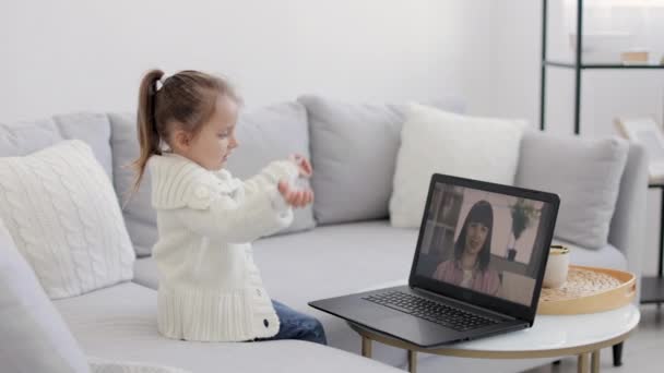 Back view of young girl sitting and relaxing on sofa at home and talking on video call with smiling mother. — Vídeo de Stock