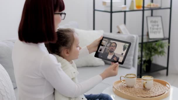 Mother and her daughter sitting and relaxing on sofa at home and talking on video call with smiling father — Vídeo de Stock