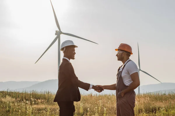 Colleagues shaking hands with wind turbines on background — Zdjęcie stockowe