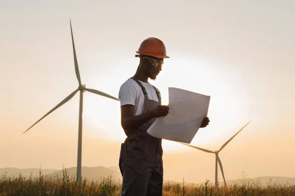 Engineer with blueprints standing among windmill farm — Zdjęcie stockowe