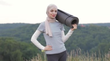 Tesettürlü ve spor elbiseli bir kadın gülümsüyor ve işaret veriyor.