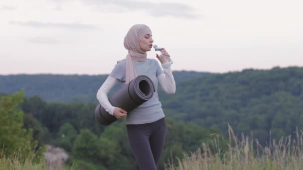 Vrouw in hijab en activewear drinkwater in het park — Stockvideo