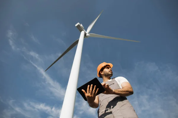 Inżynier indyjski stojący wśród farmy wiatraków z tabletem — Zdjęcie stockowe