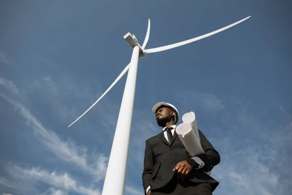 Człowiek w garniturze stojący pośród wiatraków z planami — Zdjęcie stockowe
