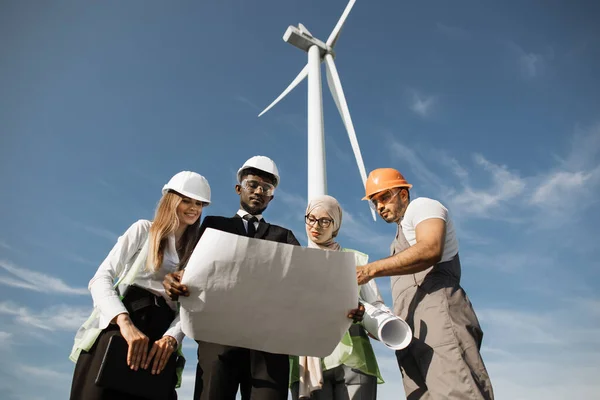 Czterech partnerów w kaskach studiujących plany turbin wiatrowych — Zdjęcie stockowe